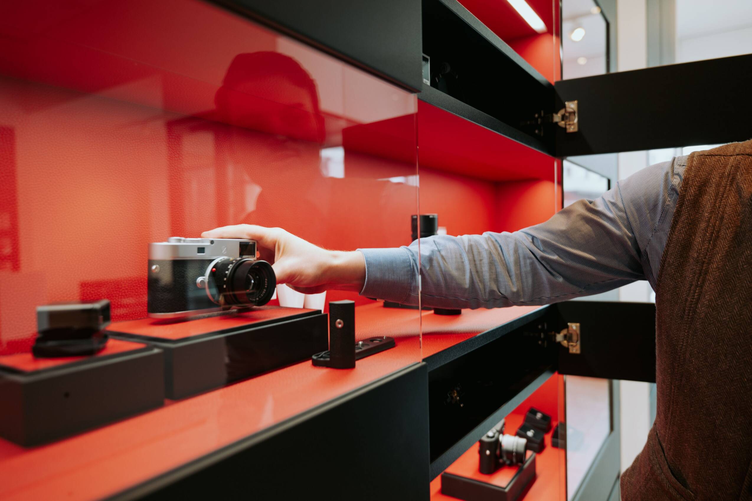 An employee at the Leica Store Wetzlar reaches for a Leica camera that is in the display cabinet.