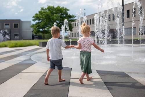 Zwei Kinder laufen Hand in Hand in der Leica Welt auf den Springbrunnen zu.