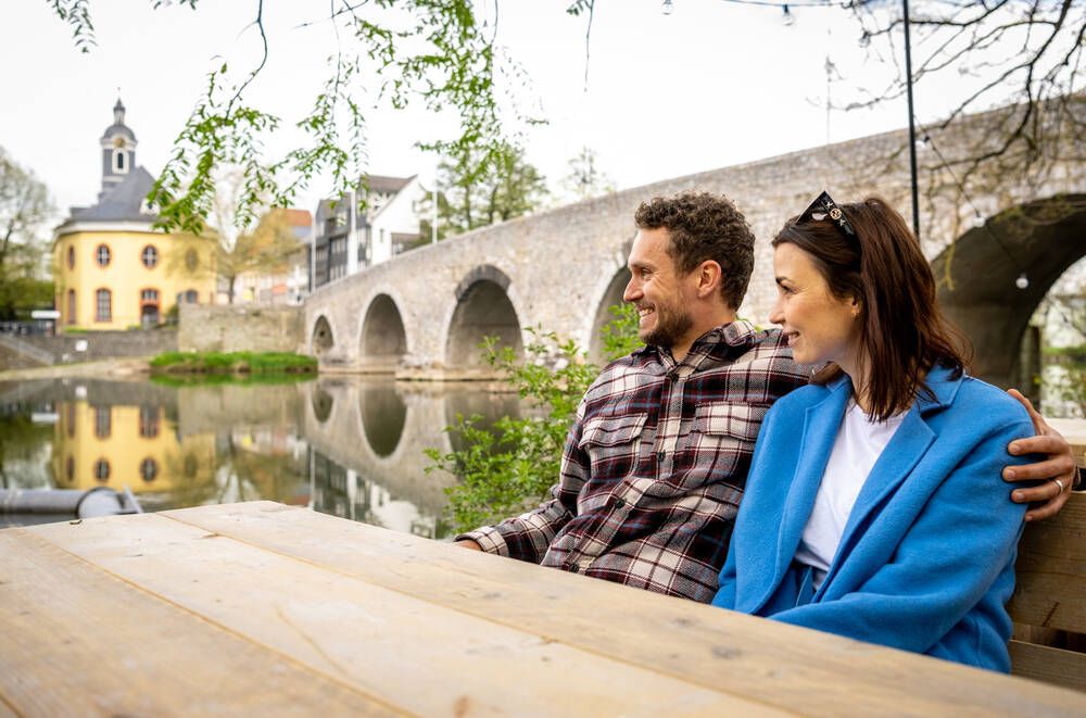 zwei Personen sitzen in einem Weingarten am Lahnufer in Wetzlar und blicken auf den Fluss.
