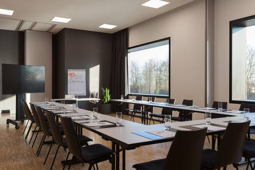 Meetingraum mit eingedeckten Tischen und großen Fenstern.